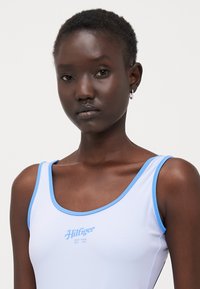Maillot de bain bleu clair. Tissu doux avec une finition mate. Présente un col en forme deU et un bord bleu contrastant. Petit logo en texte au centre.