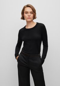 Svart langermet genser med rund hals, laget av mykt strikket stoff, kombinert med svarte skreddersydde bukser med en glatt midje.