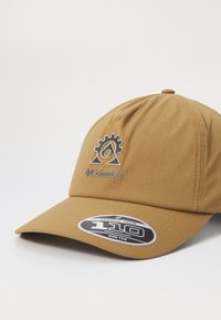 Brun kasket med struktureret stof, logo på fronten med geardesign og et cirkulært klistermærke, der angiver Flexfit-teknologi.