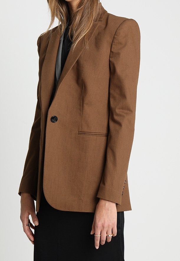 Blazer marrone su misura con spalline, chiusura a bottone singolo e due tasche laterali. Tessuto liscio, design strutturato e maniche lunghe.