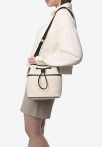 Bolsa de cubo blanca de lona con ribete negro y correa ajustable, que cuenta con un cierre de cordón y superficie texturizada.