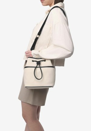 Sac seau en toile blanche avec une bordure noire et une bandoulière ajustable, doté d'une fermeture à cordon et d'une surface texturée.