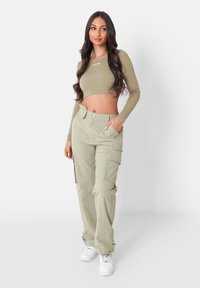 Lichtgroene cropped lange mouwen top in combinatie met lichtgroene cargobroek. De broek heeft zijzakken en manchetten met verstelbare hardware. Witte sneakers.