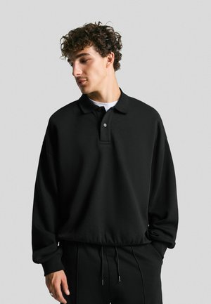 Black oversized polo sweatshirt with a fold-down collar, three-button placket, and ribbed cuffs. Smooth fabric with a relaxed fit.