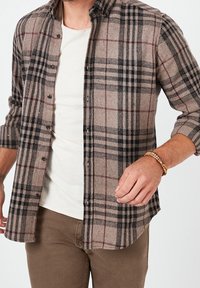 Kostkovaná flanelová košile v béžové, černé a burgundské barvě, s knoflíkovým zapínáním vpředu, dlouhými rukávy a volným střihem. Měkká textura.