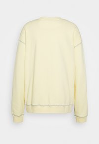 Zachte gele langemouw sweatshirt met zichtbare naden over de schouders, boorden en zoom, weergegeven vanaf de achterkant op een effen achtergrond.