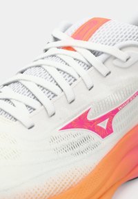 White athletic shoe with a textured upper, orange sole, pink logo accent, and reflective details. Features mesh for breathability.