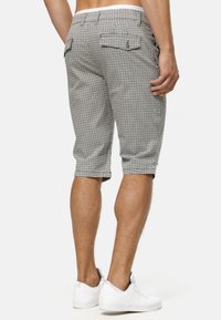 Black and white checkered shorts with a rolled hem, two back pockets, and a button detail. Paired with white sneakers.