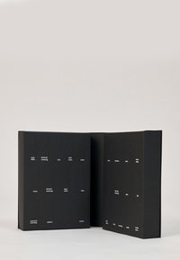 Scatola nera con sezioni ritagliate che mostrano testo bianco. Il design presenta una forma piatta robusta con una superficie liscia e un layout minimalista.