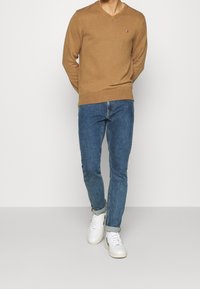 Ruskea v-kuvioinen neule pehmeästä materiaalista, yhdistettynä sinisiin farkkuihin. Valkoisissa tennareissa on teksturoitu pinta ja käännetyt hihnat.