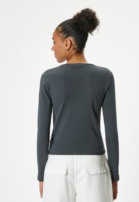 Lange mouwen, donkergrijs shirt met een aansluitend ontwerp, gemaakt van zachte stof. Het heeft een ronde halslijn en een gladde textuur. Gekoesterd met witte broeken.