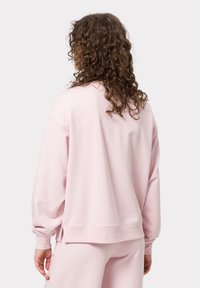 Růžová bavlněná mikina s volným střihem, žebrovanými manžetami a lemem. Hladká textura, s jednoduchým designem bez výraznějších vzorů a kování.