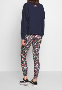 Marinblå oversized sweatshirt med korta ärmar, kombinerad med svarta leggings med ett färgglatt blommönster. Svarta sneakers fulländar outfiten.