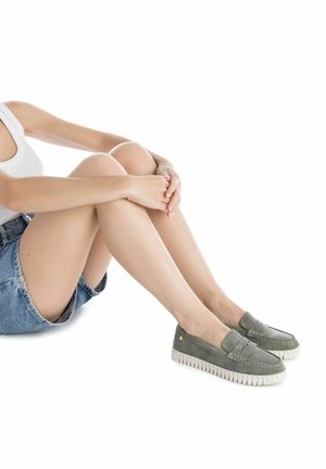 Mocasines de ante verde con suelas de goma blanca, con detalles de costura y un diseño de fácil puesta. Llevados con una falda de mezclilla.