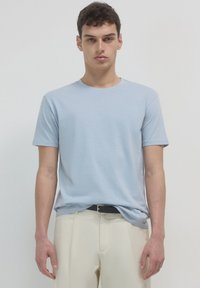 Maglietta azzurra chiara a maniche corte in tessuto morbido, colletto rotondo, abbinata a pantaloni beige chiaro e una cintura nera. Design semplice e minimal.