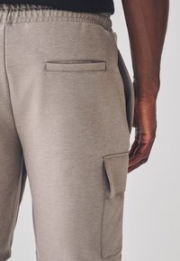 Pantaloncini da ginnastica beige realizzati in tessuto morbido, con tasca cargo laterale, vita elasticizzata e texture liscia.