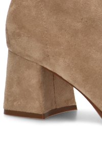 Tacón bloque de ante beige con forma cuadrada. Textura suave, que presenta un diseño ligeramente cónico y una base plana para mayor estabilidad.