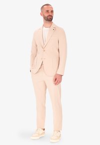 Completo beige su misura con due bottoni, design a un solo petto, revers a punta e tasche laterali, abbinato a sneakers beige e t-shirt bianca.