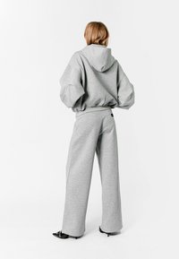 Sudadera gris oversized con capucha y mangas anchas, combinada con pantalones grises holgados a juego, que presentan una cintura alta y piernas rectas.