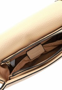 Beige nahk käekoti sisemus, millel on sile tekstuur, sisaldab lukuga jaotust ja beeži voodri. Kaks lukku ja silt on nähtavad.