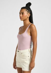 Ribbet, lyserød tanktop med brede stropper i skulderen, parret med cremefarvede, højtaljede shorts, der har forlommer og knapdetalje.