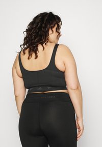 Top desportivo preto com textura ribada e alças largas, combinado com leggings altas pretas que apresentam um logótipo simples na cintura.