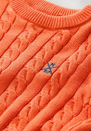 Narančasti pleteni pulover s teksturiranim uzorkom pletenice, rebrastim izrezom i malim plavim logotipom u središtu.