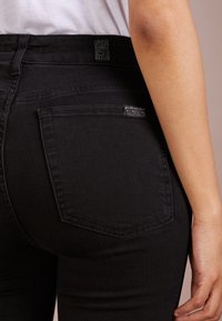Černé džínové kalhoty s přiléhavým střihem, zadními kapsami s prošíváním a texturovanou černou nášivkou na pasu.