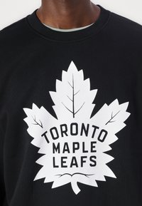 Hanorac negru cu un grafic alb în formă de frunză de arțar și textul "TORONTO MAPLE LEAFS". Culoare cu guler ribelat, material din bumbac, textură netedă.