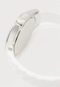Montre en acier argenté avec couronne et fond fermé, fixée à un bracelet en silicone blanc texturé.