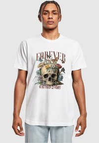 Hvit bomulls t-skjorte med et grafisk design av et skjelett omgitt av blomster og sommerfugler, med tekst som sier "For alltid og alltid" og "Grip dagen."