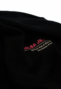 Tela negra con un tejido texturizado presenta un logo impreso en rosa y dorado que dice "SALSA JEANS" y la frase "Diferente tipo de denim azul."