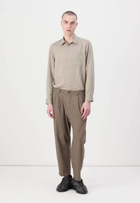 Lyst brunt stripete langermet skjorte med en lomme, kombinert med løse brune bukser og mørke sneakers, med en avslappet passform.