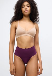 Γυμνό σουτιέν bralette με λεπτές τιράντες και βαθύ V, συνδυασμένο με σκούρο μωβ σλιπ χωρίς ραφές και ψηλή μέση, με ομαλή υφή.