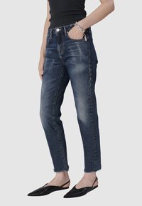 Jean en denim bleu foncé avec une coupe slim, légère décoloration et ourlets effilochés, assortis à des ballerines noires à bout pointu.