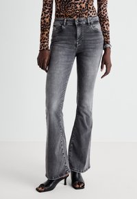 Grijze flared jeans van denim, met vijf zakken, medium wassing en subtiele vervaging, gecombineerd met zwarte open teen hakken.