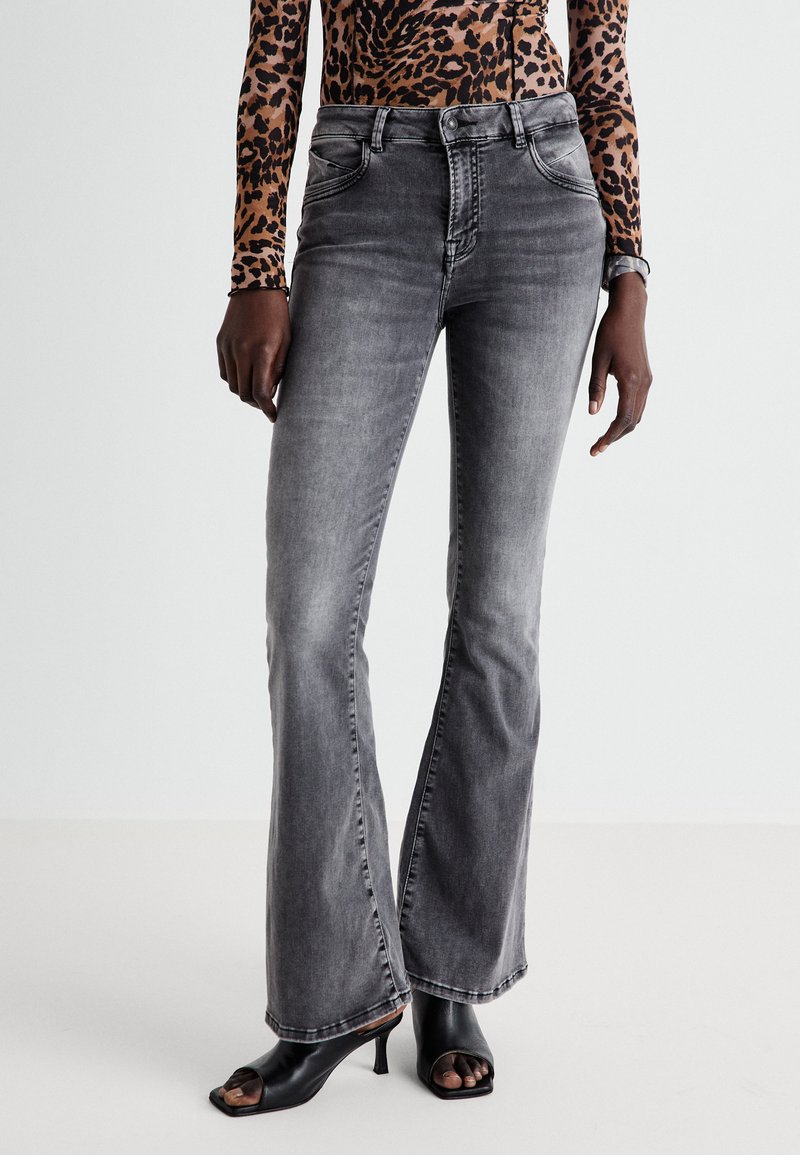 Grijze flared jeans van denim, met vijf zakken, medium wassing en subtiele vervaging, gecombineerd met zwarte open teen hakken.