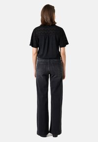 Schwarzes Kurzarmtop mit Spitze und lockerer Passform, kombiniert mit hochgeschnittenen, weitgeschnittenen schwarzen Jeans mit Gesäßtaschen.