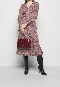 Czerwona sukienka w wzór paisley z długimi rękawami, w połączeniu z pikowaną bordową torebką na łańcuszku w kolorze złotym oraz czarnymi, zwężającymi się kozakami do kolan.
