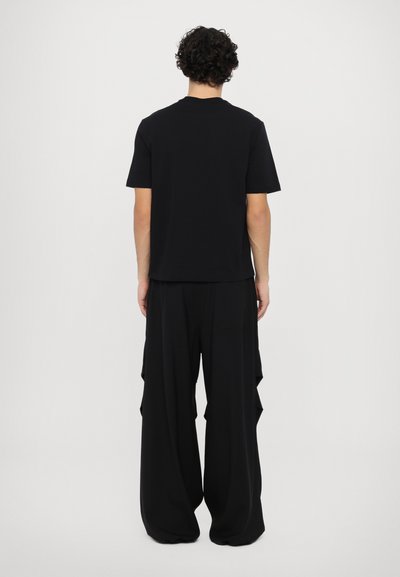 Black t-shirt with short sleeves, paired with wide, flowing black pants featuring layered design and side pockets.