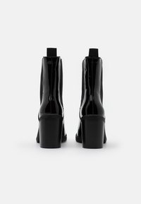Stivaletti alla caviglia in vernice nera con un design elegante, punte arrotondate e un tacco spesso e testurizzato. Presentano lati elastici per un facile indossamento.