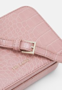 Rožinė krokodilo odos piniginė su auksine sagtimi ir "TED BAKER" logotipu. Savybės: sklandi tekstūra ir siuvinėtos kraštai.