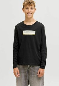 Zwarte langetermijn T-shirt met een rechthoekig logo waarin "JACK & JONES" en "SINCE NINETEEN NINETY" in witte en gouden tekst zijn weergegeven, gecombineerd met grijze spijkerbroek.