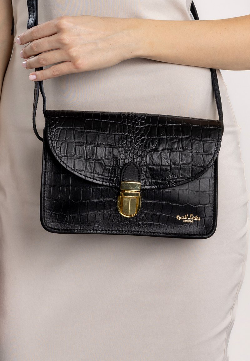 Schultertasche aus schwarzem Krokodil-Prägung-Leder mit Klappenverschluss und goldenen Hardware-Details. Verstellbarer Tragegurt. Strukturierte Oberflächendetails.