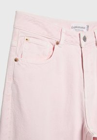 Jean en denim rose clair avec poches avant, rivets en métal et une étiquette de marque Stradivarius ainsi qu'une étiquette de taille visibles à l'intérieur de la ceinture.