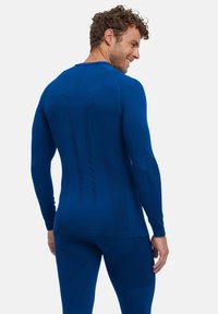 Chemise de sport bleu à manches longues avec des panneaux texturés dans le dos et sur les manches. Coupe ajustée, fabriquée à partir d'un matériau extensible, offrant une flexibilité.