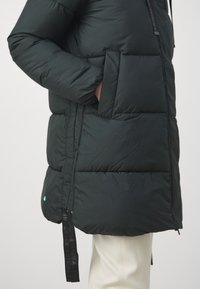 Black puffer jacket with a textured finish, featuring a large pocket, side zippers, and an accent strap on the hem. Insulated design.