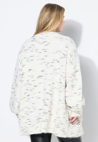 Krämfärgad oversized tröja med texturerat stickat mönster och subtila grå prickar. Har sänkt axlar och ribbade ärmslut.