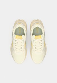 Light beige athletic shoes with yellow accents. Mesh and synthetic upper, padded collar, flat laces, and textured rubber sole.