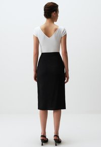 Zwarte knielange rok met een textuurafwerking, gecombineerd met een aansluitend wit geribd topje met een diepe V-rug. Zwarte hakken maken de look af.